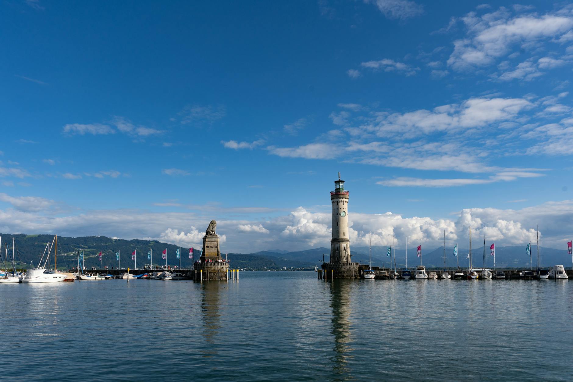 Beautiful view of Lindau Harbor with iconic lighthouse and statue, surrounded by calm lake waters.