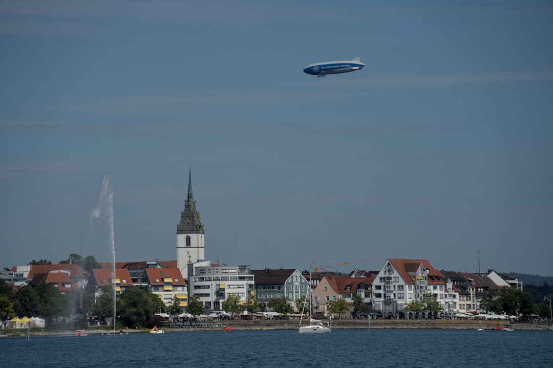 Zeppelin flies over a coastal town with a fountain.