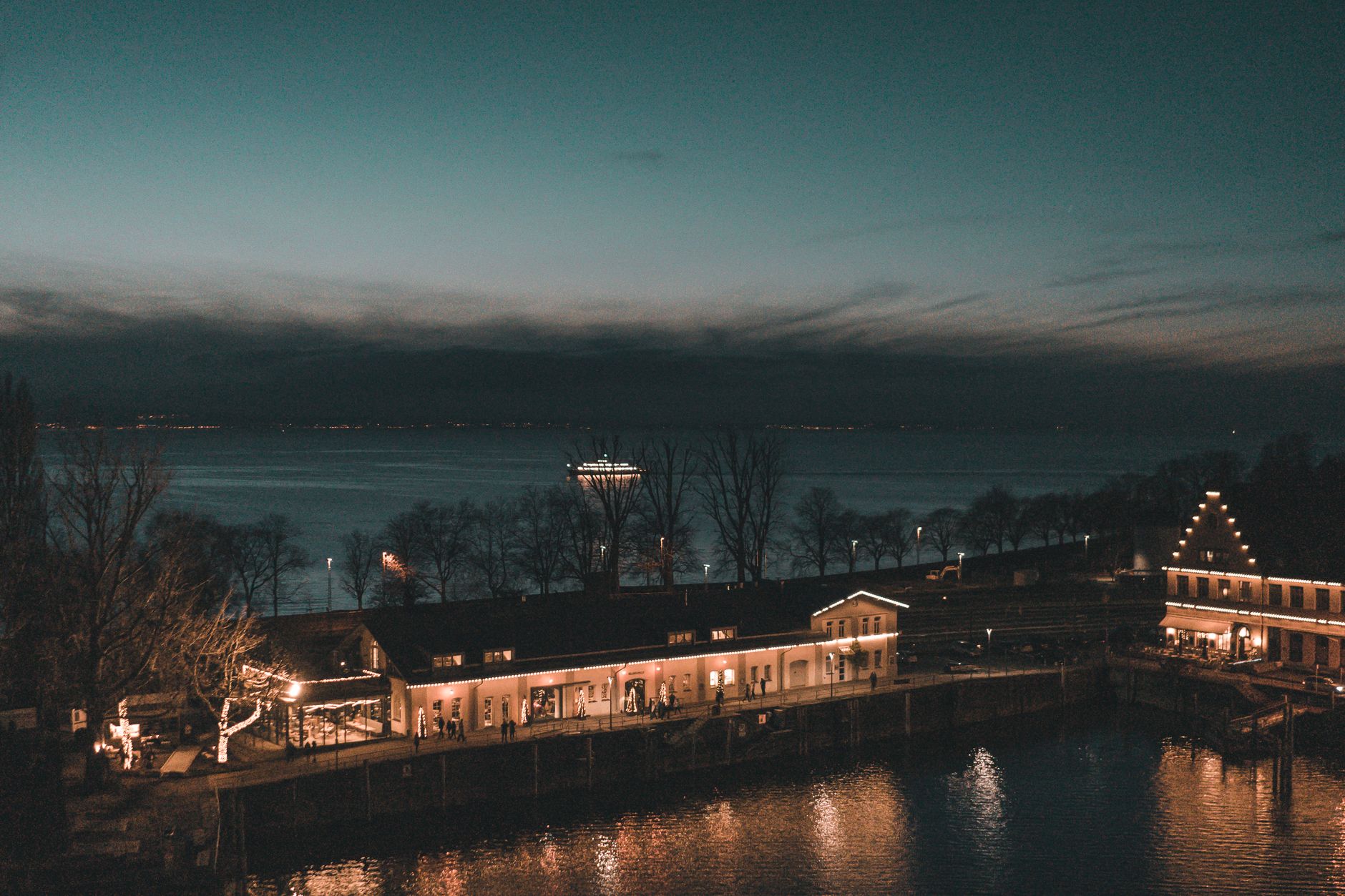 Twilight at Lindau's lakeshore with illuminated buildings and trees lined by Lake Constance.