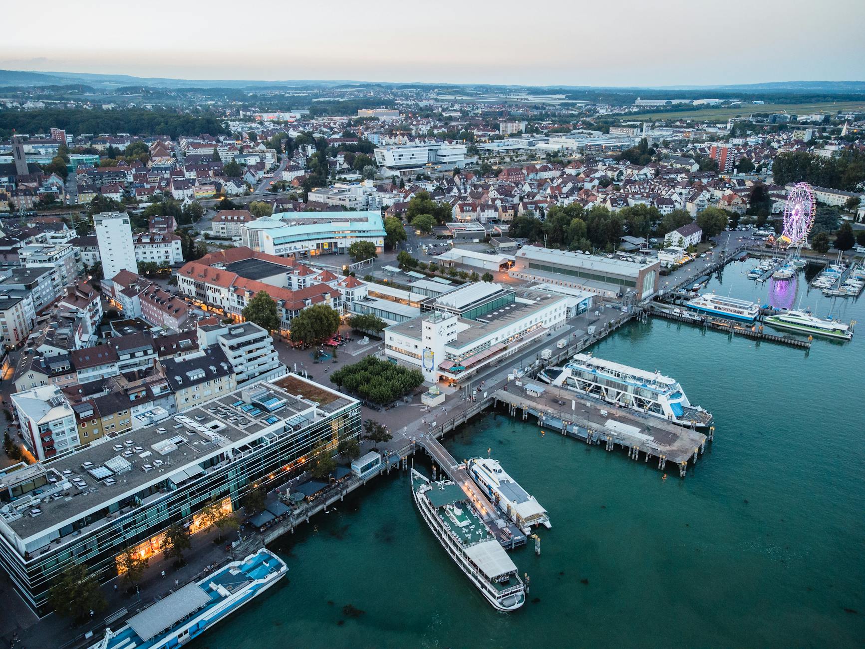 Beautiful aerial shot of Friedrichshafen, Germany, showcasing the waterfront, cityscape, and ferris wheel at dusk.
