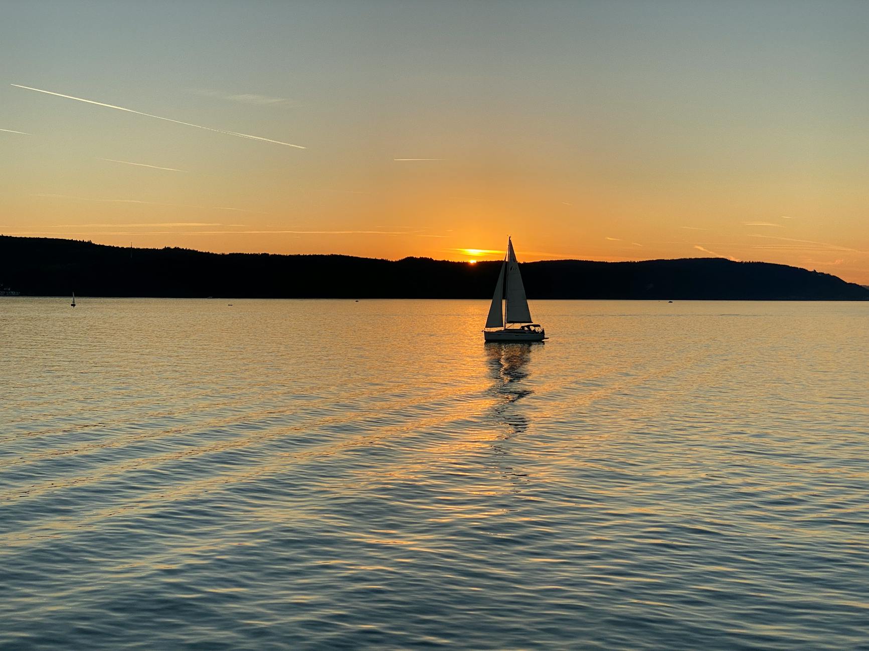 A tranquil sailboat glides on a serene lake in Überlingen during a beautiful sunset.