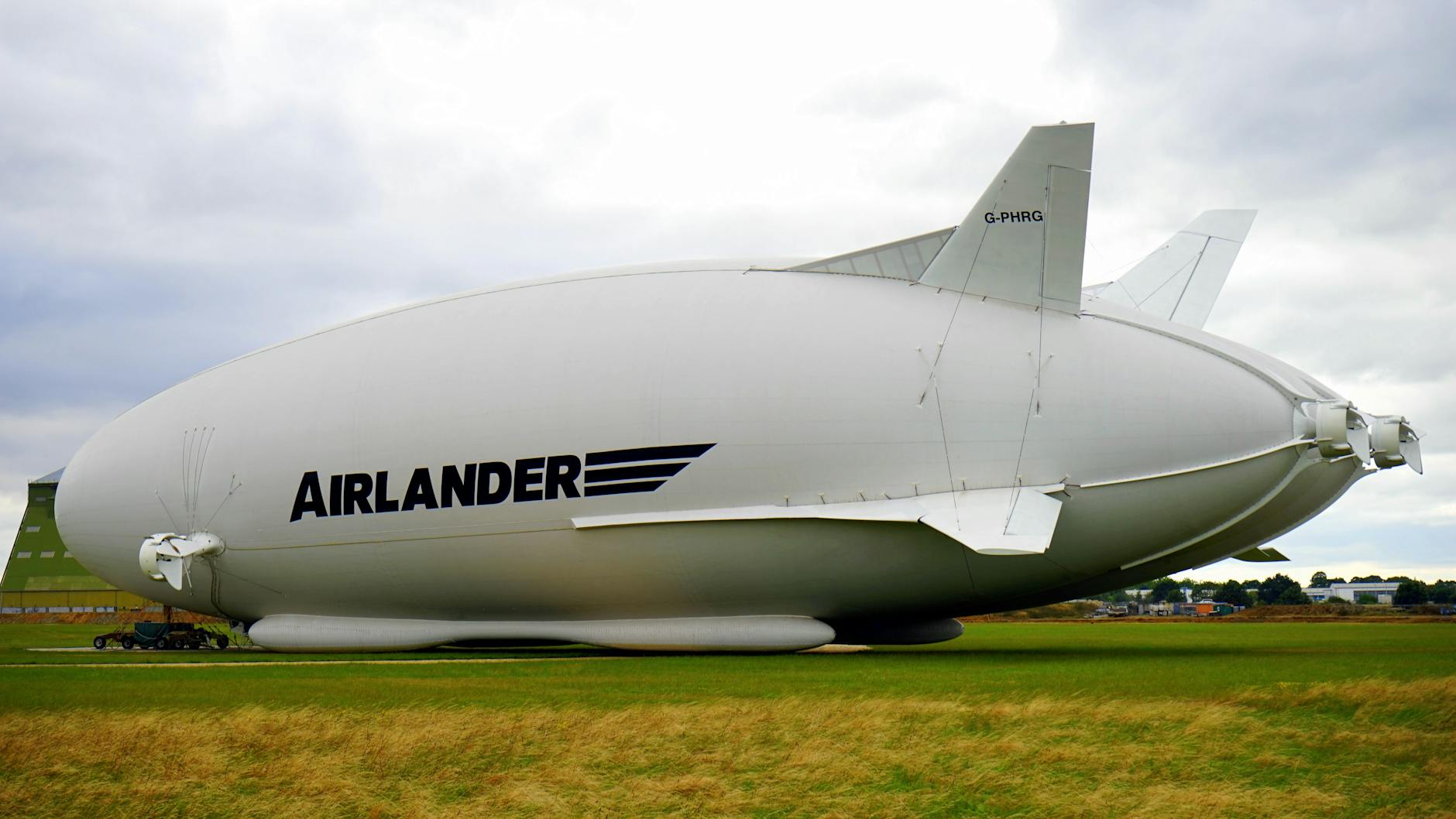 A large Airlander hybrid airship parked on a grassy field under a cloudy sky.