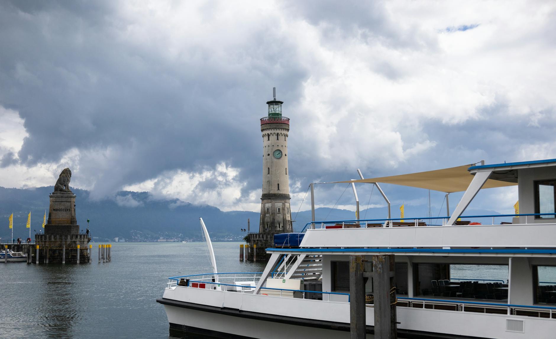 View of Lindau Lighthouse and a boat at Lake Constance under cloudy skies.