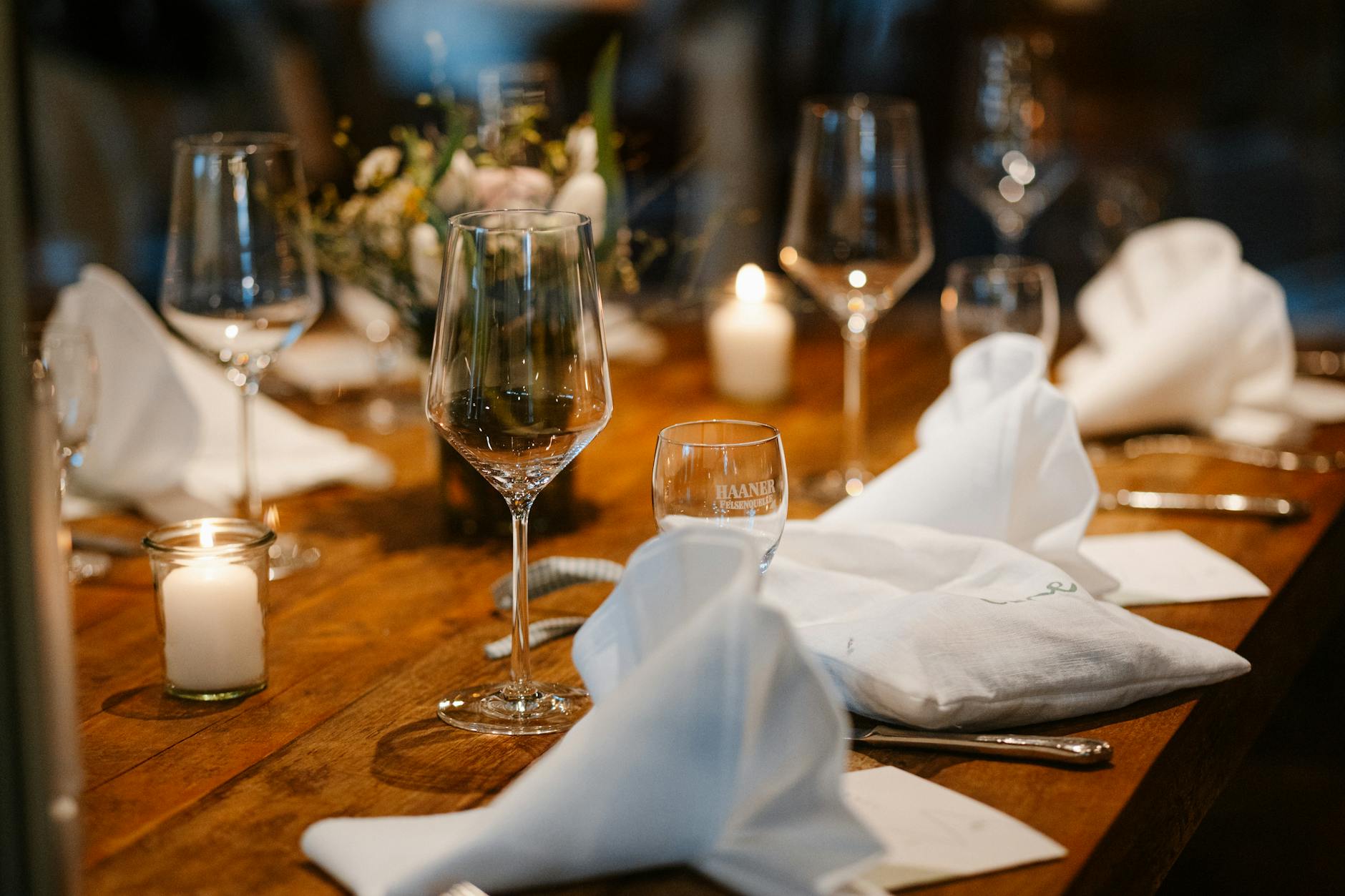 Cozy restaurant table set with glassware, white napkins, and candles.