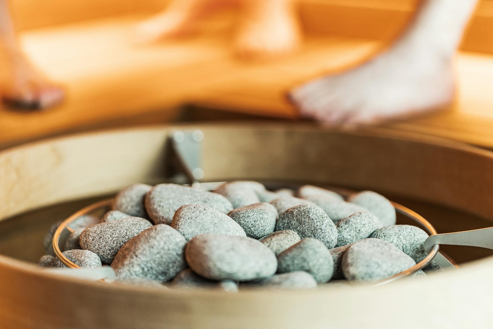 Close-up of sauna stones with blurred feet in a warm, indoor sauna setting.