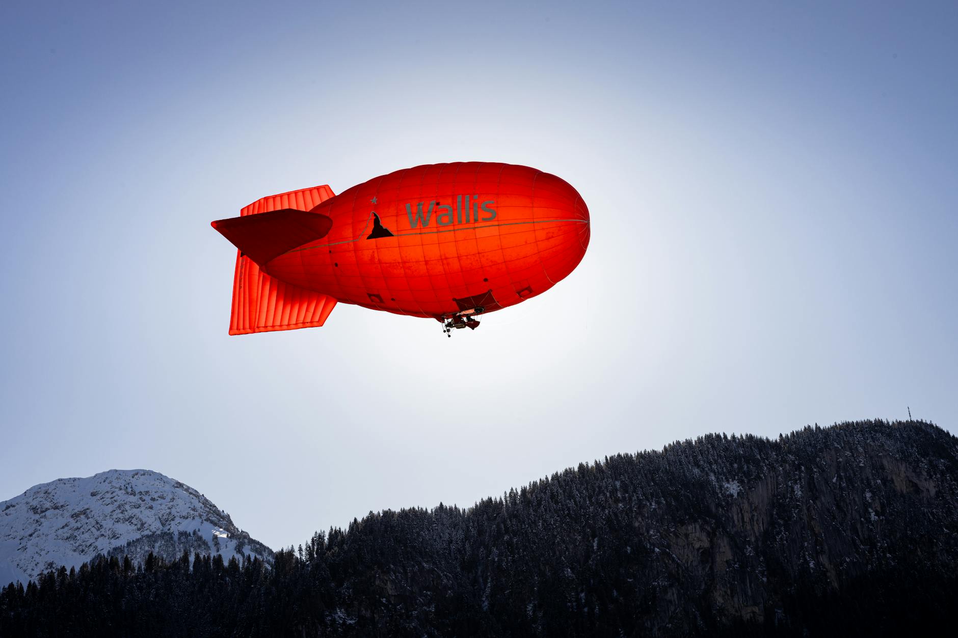 Red blimp floats over snowy peaks in Château-d'Oex, capturing a serene aerial view.