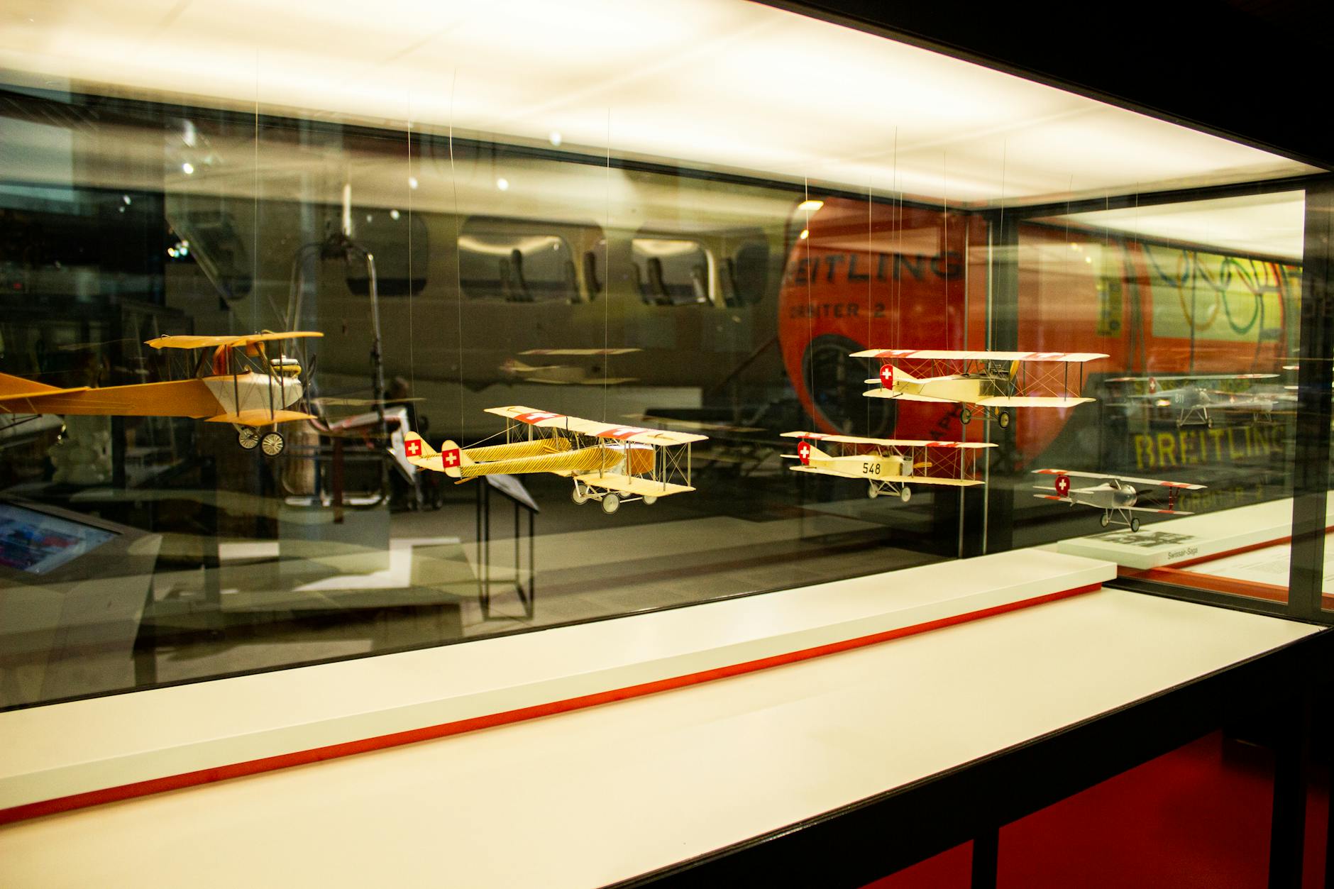 Showcase of vintage model airplanes in a Swiss museum with reflective glass.