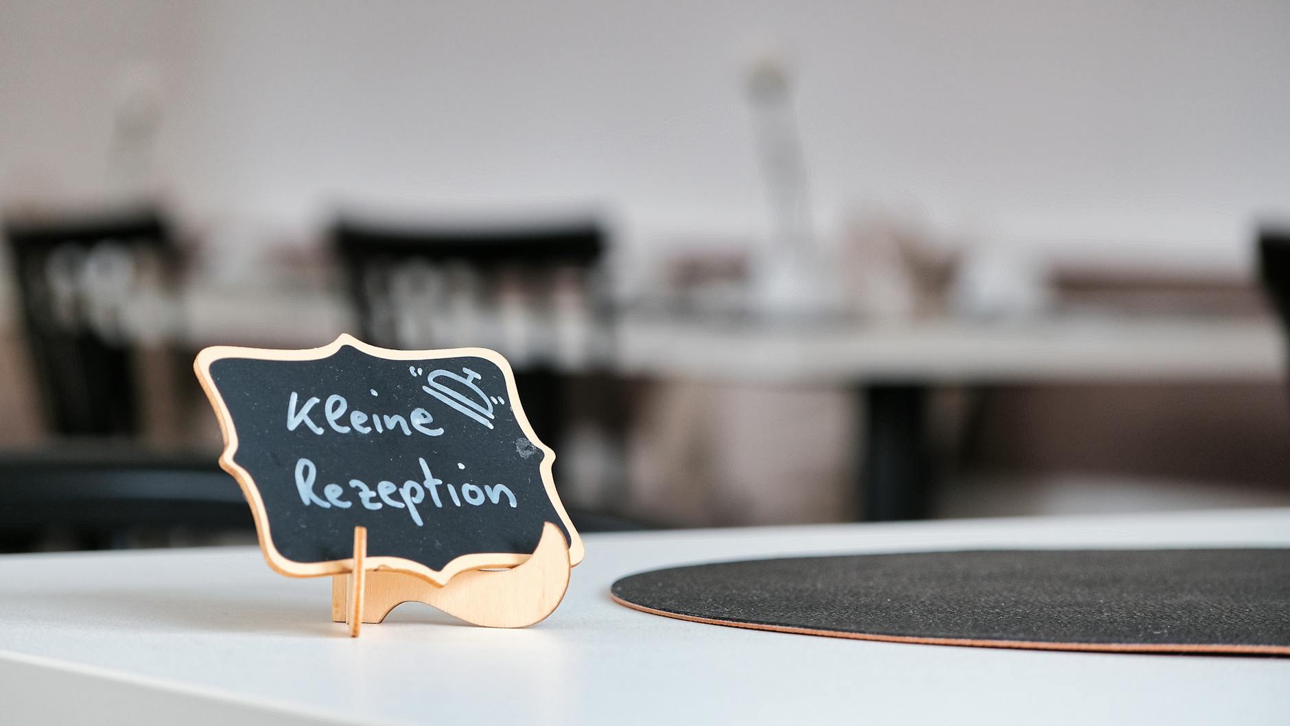 Chalkboard sign reading 'Kleine Rezeption' on a restaurant table, perfect for cozy dining ambiance.