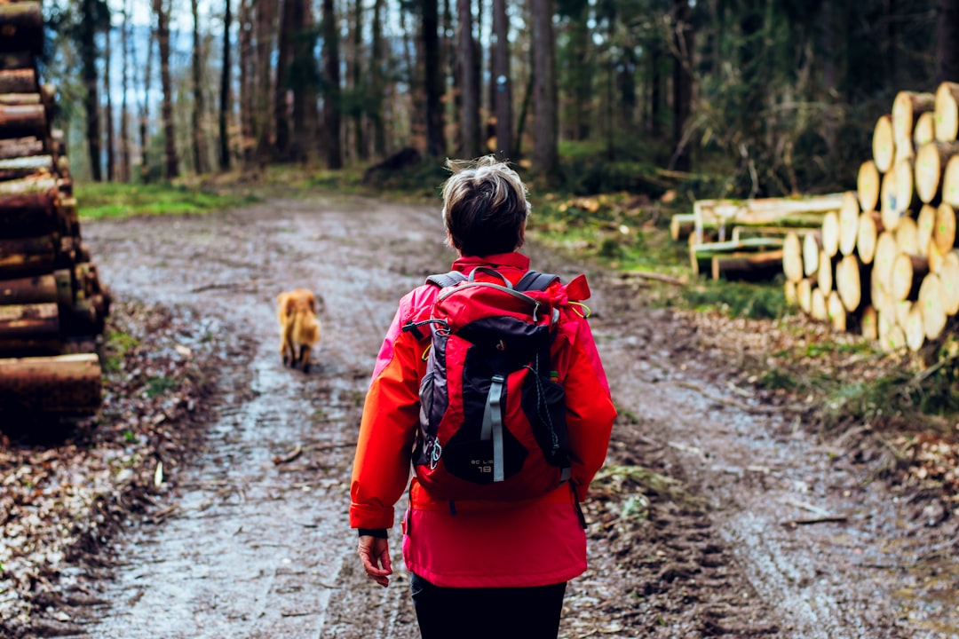 woman in red and black jacket walking with brown dog on pathway during daytime