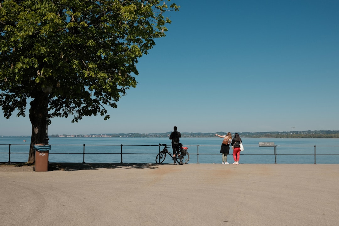 People with a bike stand by a calm lake.