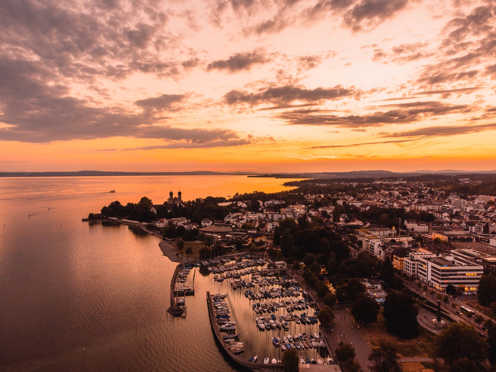 A stunning aerial view of Friedrichshafen, Germany during a dramatic golden hour sunset by the waterfront.