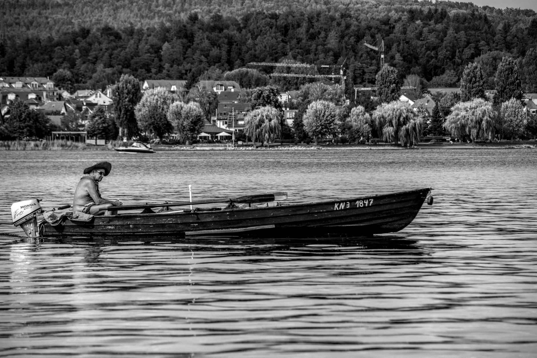 Monochrome image of a lone man on a boat in Lake Constance near scenic shoreline.