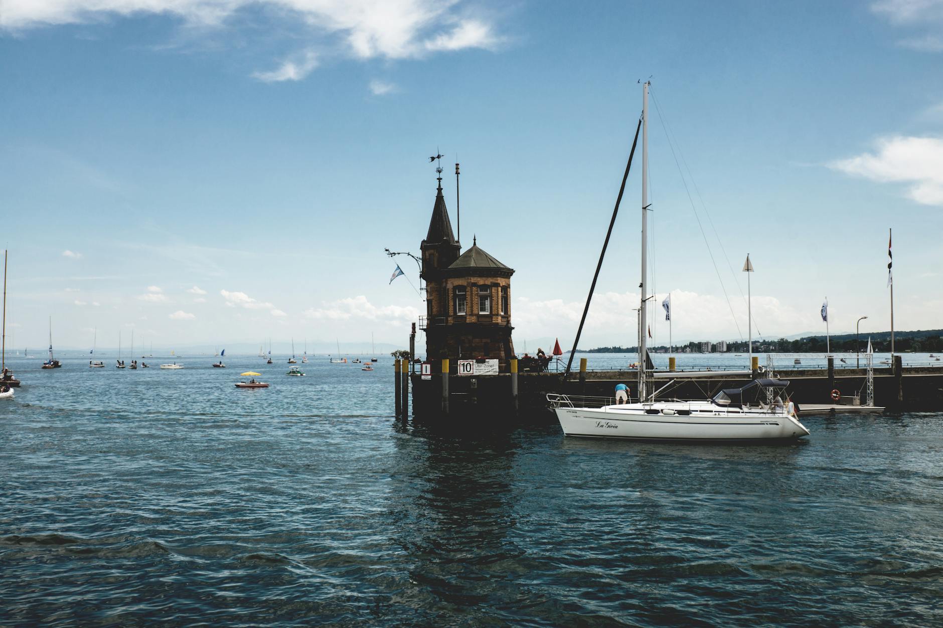 Charming view of sailboats and the iconic harbor tower in Konstanz, Germany on a sunny day.