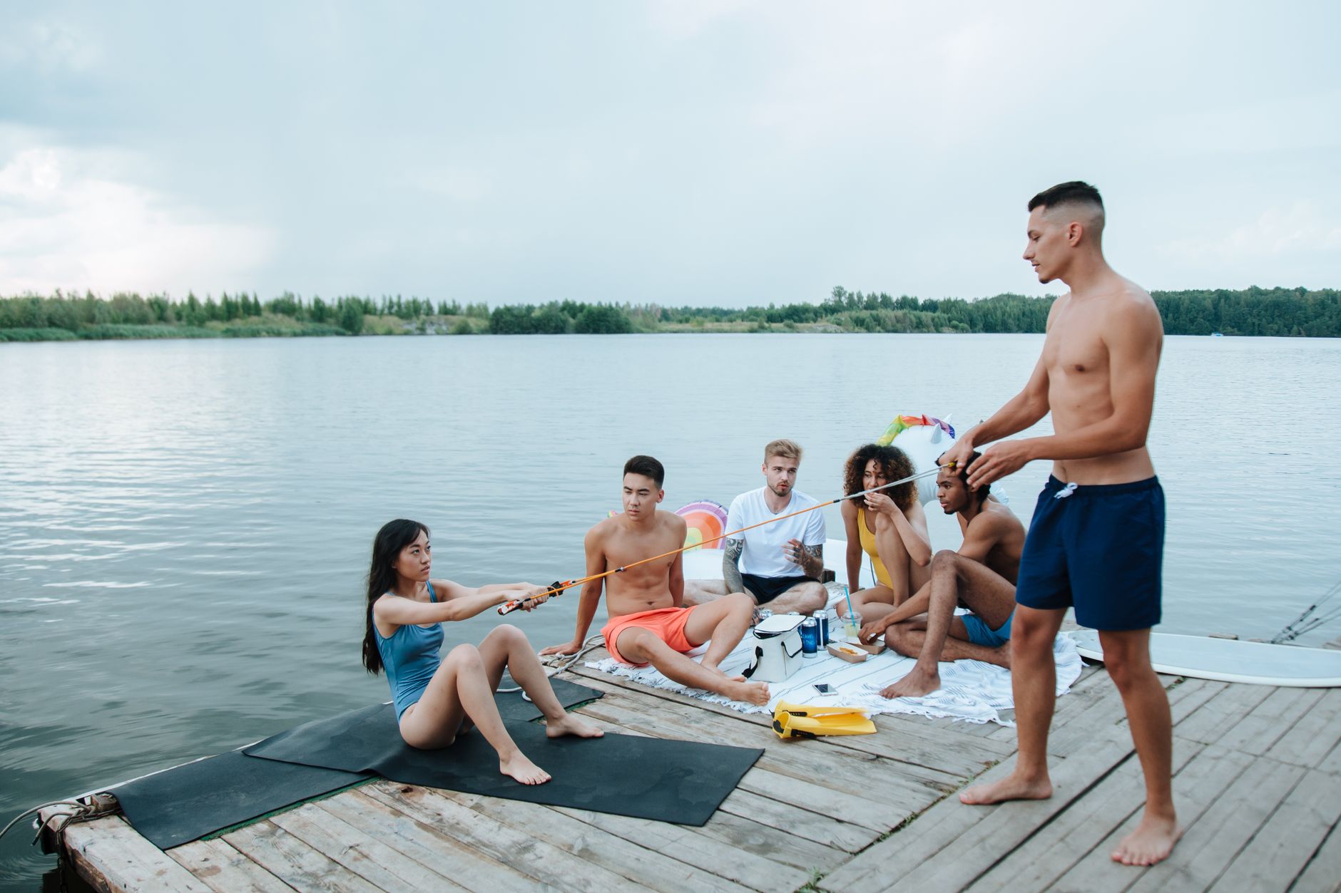 A diverse group of friends enjoys a summer day socializing by the lake on a wooden pier.