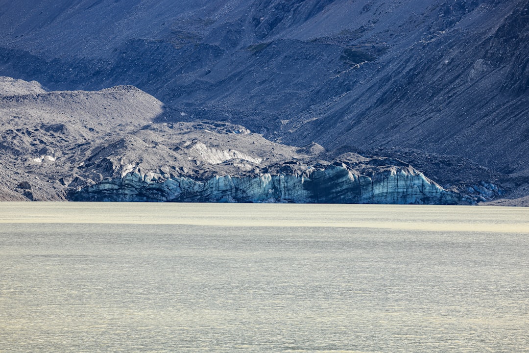 Glacier calving into a pale lake with mountains behind.